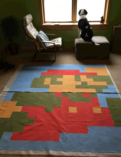 An animated GIF of Liam the dog walking on the quilt, sitting down, and yawning.