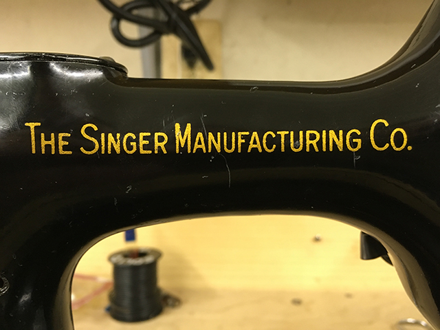 A closeup of the decal on the back of the sewing machine arm. It reads, "The Singer Manufacturing Co."