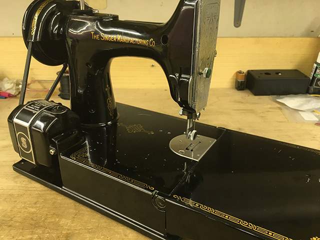 A rear view of the sewing machine. The motor is on the left and a decal on the machine arm reads "The Singer Manufacturing Co."