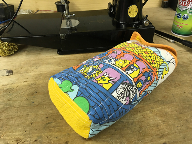 A small quilted bag sits in front of the sewing machine. It has a colorful Noah's ark pattern on it.
