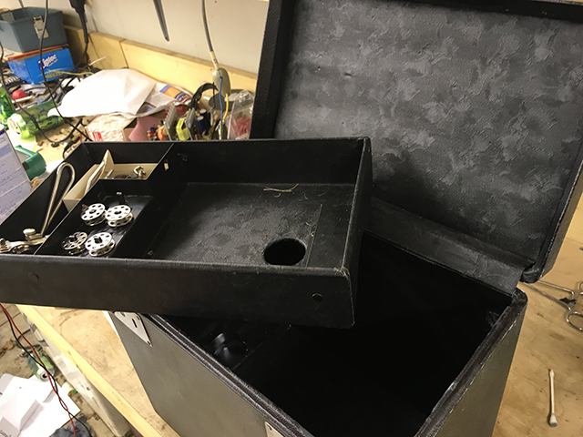 A tray sits on top of the open case. It has a storage compartment on the left side for bobbins and other notions and the right side has a hole in the bottom to accomodate the thread spool.