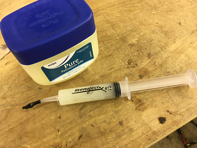 A picture of a tub of petroleum jelly. Beside it is a Monoject 412 plastic syringe filled with petroleum jelly.