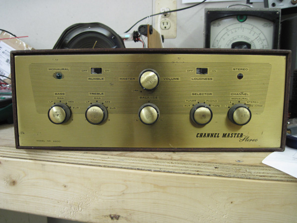 A view of the front of the amp, which is solid brass. There are six knobs (power/volume, bass, treble, balance, input selector, and channel selector), two slide switches (rumble and loudness), and two lamps with jewels (a green one for monaural and a red one for stereo.)